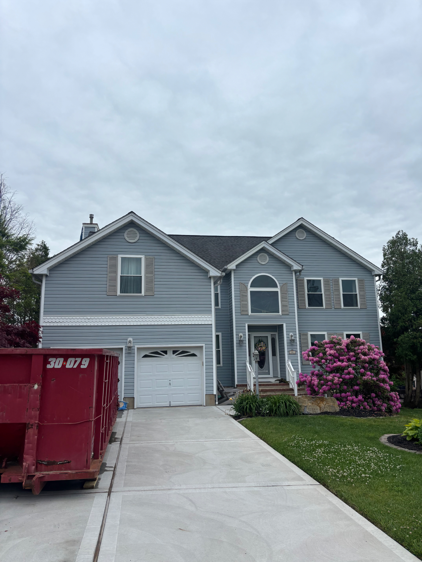 Gray shore home before new siding, with dumpster in driveway